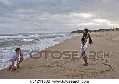 Young man on one knee on beach, young woman standing in heart shape View Large Photo Image Stock Image - Young man on one knee on beach, young woman standing in heart shape. Fotosearch