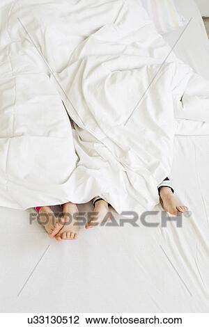 Stock Image - Young sisters feet sticking out of duvet on bed. Fotosearch