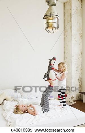 Young sisters playing with soft toy on the bed View Large Photo Image Stock Photography - Young sisters playing with soft toy on the bed. Fotosearch