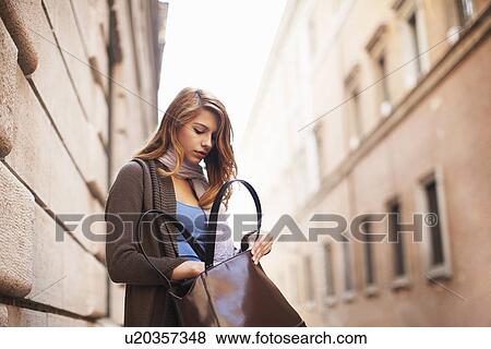 Stock Photo - Young woman anxiously searching her shoulder bag. Fotosearch