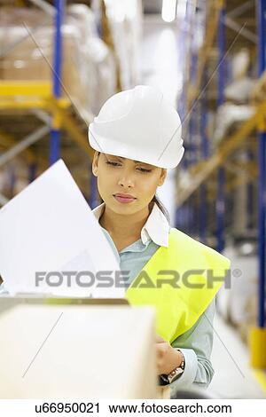 Stock Image - Young woman checking order in distribution warehouse. Fotosearch