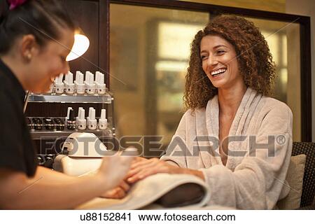 Stock Image - Young woman enjoying nail manicure in spa. Fotosearch