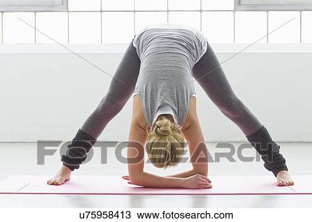 Stock Image - Young woman in yoga pose, bending forwards. Fotosearch