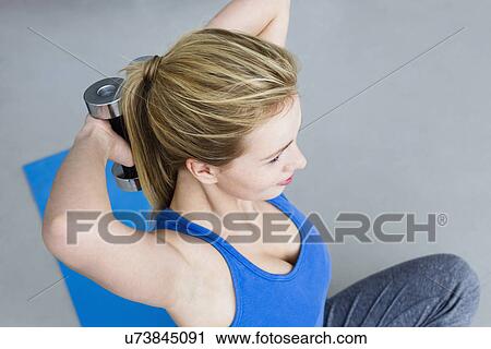 Stock Image - Young woman lifting weights. Fotosearch