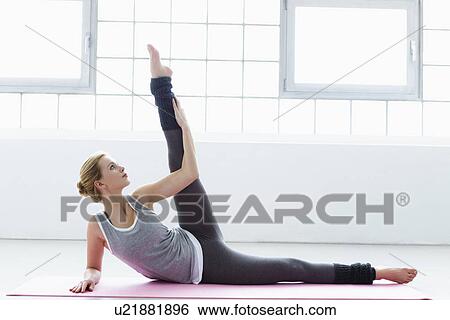Young woman lying on yoga mat, leg raised View Large Photo Image Stock Photograph - Young woman lying on yoga mat, leg raised. Fotosearch