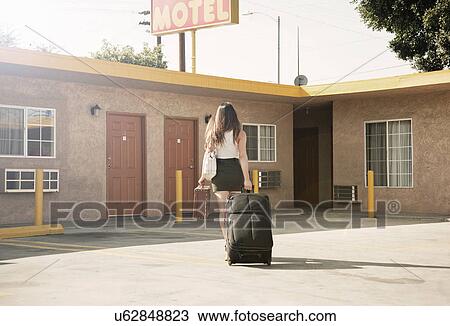 Young woman pulling wheeled suitcase outside motel, rear view View Large Photo Image Stock Image - Young woman pulling wheeled suitcase outside motel, rear view. Fotosearch