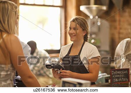 Stock Photograph - Young woman serving customer in coffee shop. Fotosearch