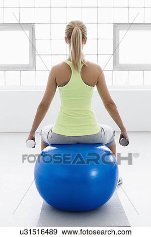 Young woman sitting on exercise ball, rear view, with weights View Large Photo Image Stock Photo - Young woman sitting on exercise ball, rear view, with weights. Fotosearch