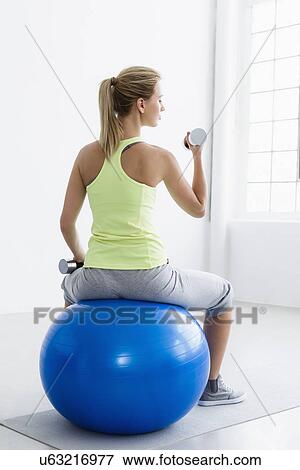 Young woman sitting on exercise ball, rear view, lifting weights View Large Photo Image Stock Photo - Young woman sitting on exercise ball, rear view, lifting weights. Fotosearch