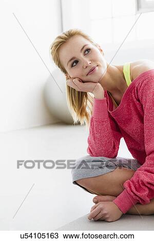 Stock Image - Young woman sitting on exercise mat. Fotosearch