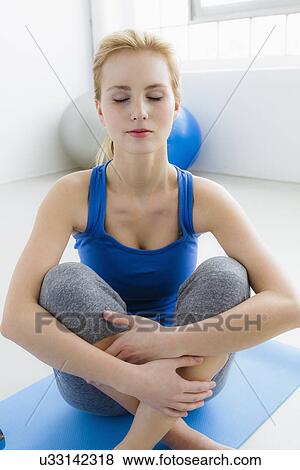 Stock Photo - Young woman sitting on exercise mat, eyes closed. Fotosearch