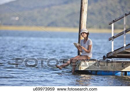 Young woman sitting on jetty, reading book View Large Photo Image Stock Photo - Young woman sitting on jetty, reading book. Fotosearch