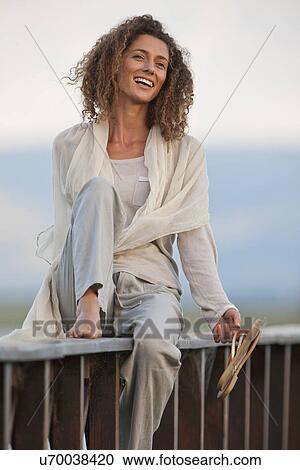Stock Image - Young woman sitting on jetty. Fotosearch