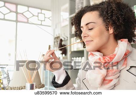 Stock Image - Young woman smelling joss sticks in boutique. Fotosearch