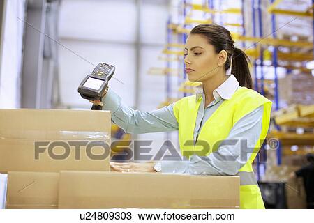 Stock Image - Young woman using barcode reader in distribution warehouse. Fotosearch