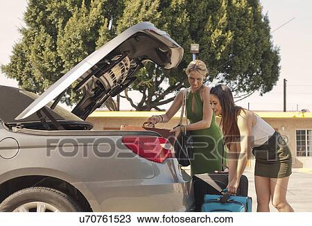 Stock Image - Young women putting suitcases into car. Fotosearch