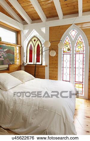 Stock Photograph - Bed with stained glass window and wooden beam ceiling at home; Taos; New Mexico; USA. Fotosearch