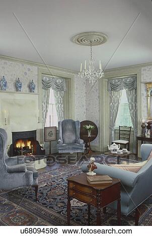 Stock Photo - Blue wing chairs with fireplace and pale blue swag curtain; in the living room. Fotosearch