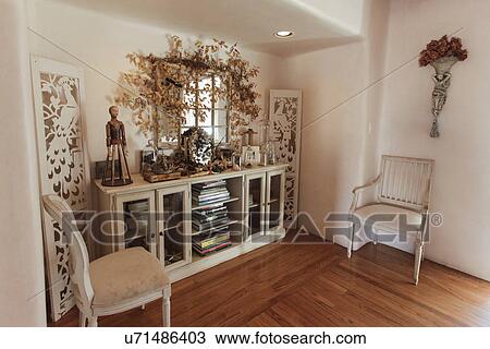 Stock Image - Books in cabinet with chairs on wooden floor at home; Santa Fe; New Mexico; USA. Fotosearch