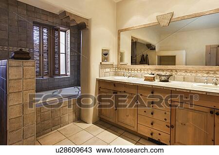 Stock Image - Brown cabinets and mirror with tiled bath in the bathroom; Santa Fe; New Mexico; USA. Fotosearch