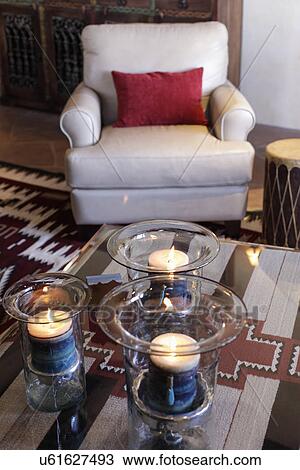 Stock Image - Close-up of lit candles on coffee table with upholstered armchair in living room; Santa Fe; New Mexico; USA. Fotosearch