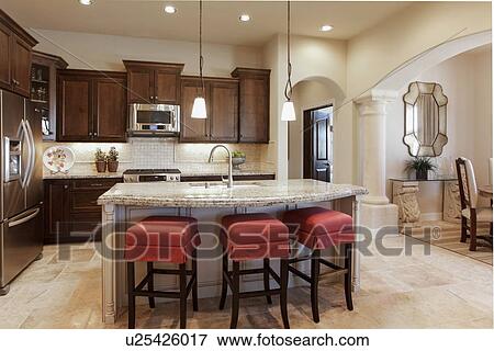 Stock Photo - Cushioned stools at the kitchen island with brown cabinets at home; Santa Fe; New Mexico; USA. Fotosearch