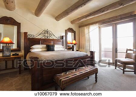 Stock Photo - Lit table lamps by tidy bed with wooden beam ceiling in bedroom at home; Santa Fe; New Mexico; USA. Fotosearch