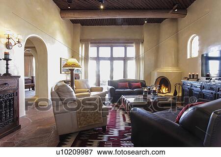 Stock Photo - Living room with seating furniture and lit fireplace at home; Santa Fe; New Mexico; USA. Fotosearch