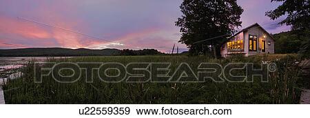 Stock Photo - Panoramic shot of an illuminated cabin with clapboard siding by lake at dusk; Burlington; Vermont; USA. Fotosearch