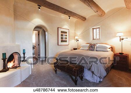 Picture - Table lamps by tidy bed with fireplace in bedroom at home; Santa Fe; New Mexico; USA. Fotosearch