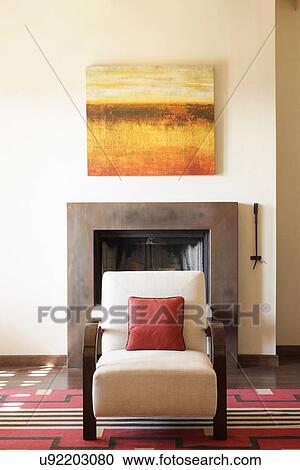 Stock Image - Upholstered chair against fireplace and painting at home; Santa Fe; New Mexico; USA. Fotosearch
