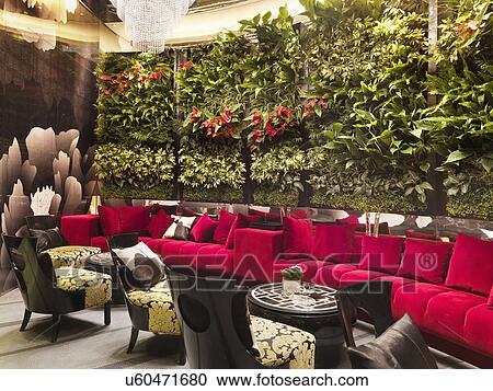Stock Image - Walled red sofa with crystal chandeliers and plants in restaurant. Fotosearch