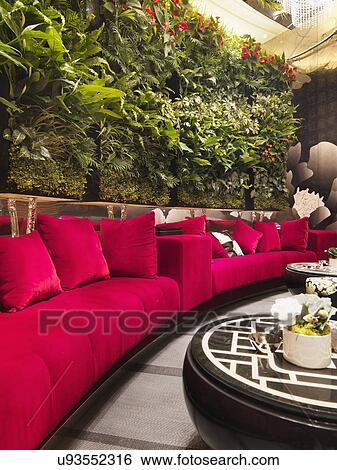 Stock Photograph - Walled red sofa with plants in restaurant. Fotosearch