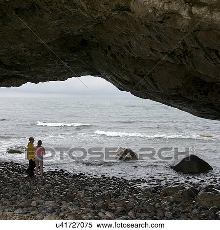 Stock Photography - Couple under natural arch on the beach, Portland Creek, Gros Morne National Park, Newfoundland And Labrador, Canada. Fotosearch