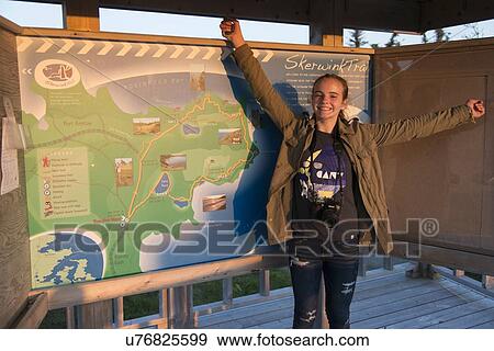 Stock Photo - Girl with arm outstretched in front of Skerwink Trail map, Bonavista Peninsula, Newfoundland And Labrador, Canada. Fotosearch