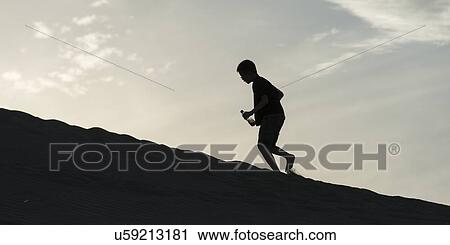 Stock Image - Person climbing on sand dune at Mingsha Shan, Dunhuang, Jiuquan, Gansu Province, China. Fotosearch