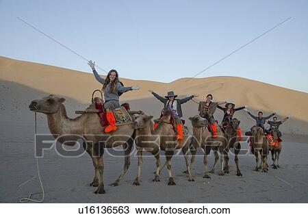 Stock Image - Tourists riding camels at Mingsha Shan, Dunhuang, Jiuquan, Gansu Province, China. Fotosearch