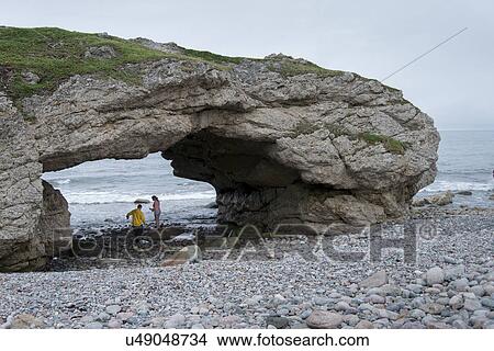 Picture - Tourists under natural arch at coast, Portland Creek, Gros Morne National Park, Newfoundland And Labrador, Canada. Fotosearch