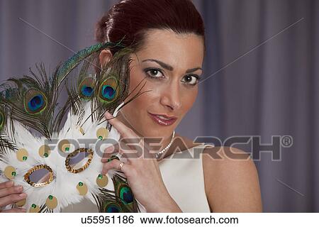 Stock Photograph - Attractive mid adult woman posing with carnival mask made of peacock feathers. Fotosearch