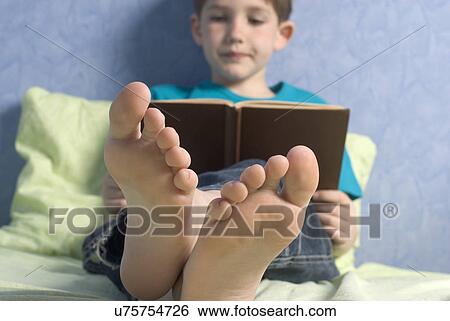 Boy (12-13) reading book on bed View Large Photo Image Stock Photograph - Boy (12-13) reading book on bed. Fotosearch