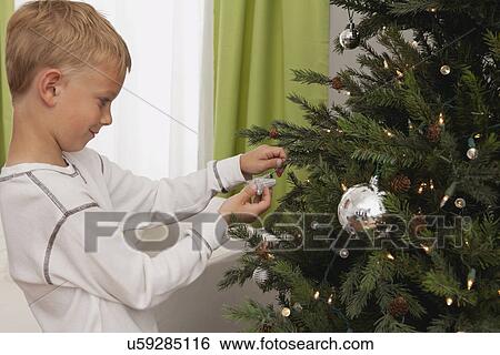 Stock Photograph - Boy (8-9) decorating christmas tree. Fotosearch