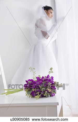Stock Photography - Bride looking out of window, flowers in foreground. Fotosearch