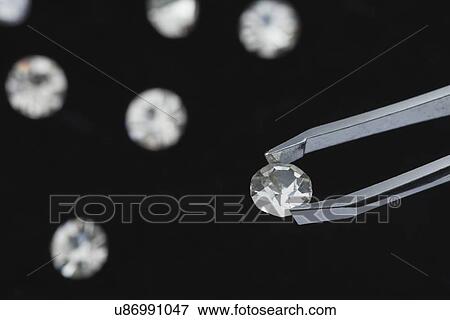 Stock Photo - Close-up of diamond holed by tweezers on black background. Fotosearch