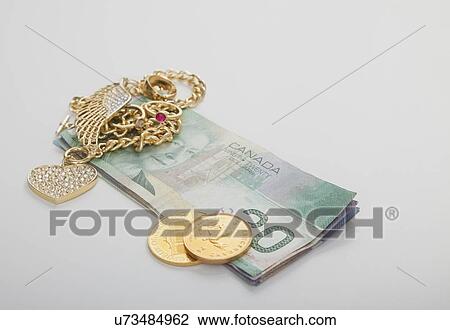 Stock Image - Close up of gold jewelry and banknotes, studio shot. Fotosearch