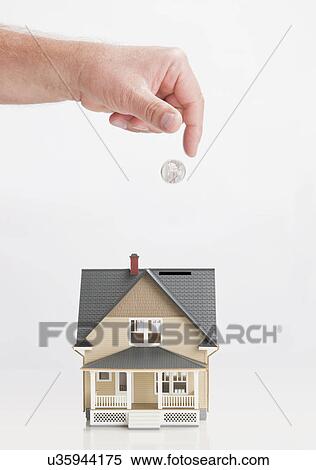 Stock Photography - Close up of man's hand throwing coin into model house. Fotosearch