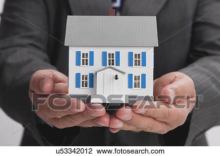 Stock Image - Close up of man's hands holding model house. Fotosearch
