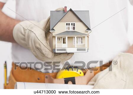 Stock Image - Close up of manual worker holding model house. Fotosearch