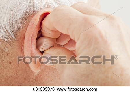 Stock Image - Close up of senior man's ear with hearing aid. Fotosearch