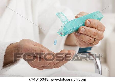 Stock Photo - Close up of senior's hands taking pill from pill organizer. Fotosearch