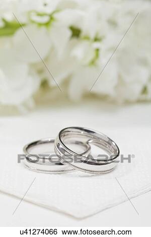 Close-up of wedding rings with white flowers in background View Large Photo Image Stock Photograph - Close-up of wedding rings with white flowers in background. Fotosearch